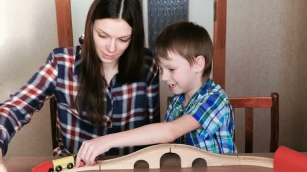 Brincando juntos. Mãe e filho estão jogando uma ferrovia de madeira com trem, vagões e túnel sentado à mesa . — Vídeo de Stock