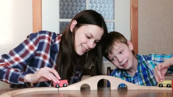 Brincando juntos. Mãe e filho estão jogando uma ferrovia de madeira com trem, vagões e túnel sentado à mesa . — Vídeo de Stock