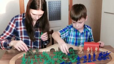 Birlikte oynayan. Anne ve oğlu ahşap bir demiryolu tren, vagonlar ve tünel ile masada oturan plastik askerler ile oynuyorlar