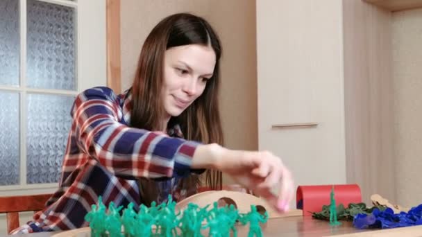 Vrouw zet plastic soldaten van verschillende kleuren op de tafel met hout spoorweg. — Stockvideo