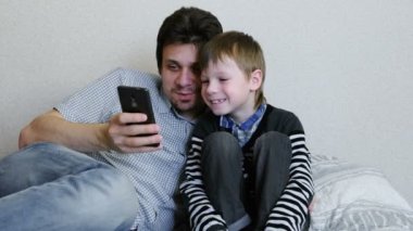 Baba ve oğul birlikte cep telefonu bir şey izliyor.
