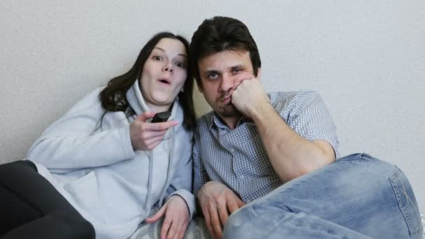 一对夫妇看电视躺在沙发上。妇女切换频道和关注和人是无聊的. — 图库视频影像