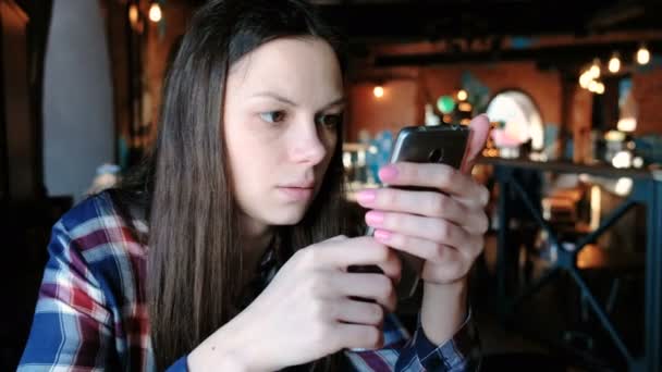 Brunett kvinna läsande något i telefonen sitter på ett café. — Stockvideo