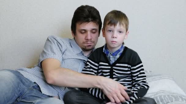 På Tv liggande på soffan. Uttråkad pojke och hans pappa tittar på Tv och växlar kanaler. — Stockvideo