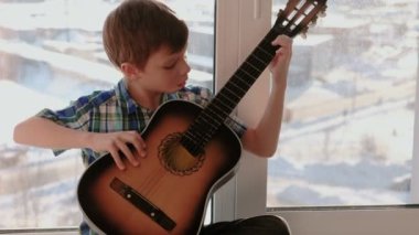 Bir enstrüman çalma. Çocuk pencere kenarında oturup gitar çalıyor.