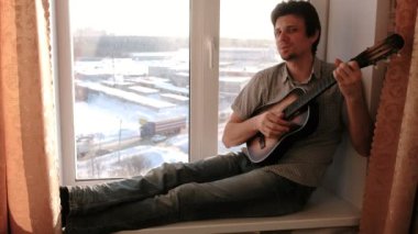 Bir enstrüman çalma. Adam pencere içinde oturan gitar çalıyor.