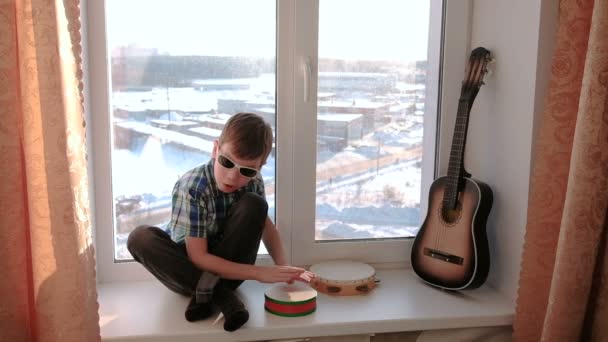 Het spelen van een muziekinstrument. Jongen speelt de trommel zitten op de vensterbank slomo — Stockvideo