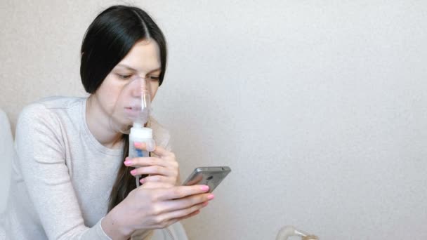 Используйте для лечения ингалятор и распылитель. Молодая женщина дышит через маску ингалятора. Вид сбоку . — стоковое видео