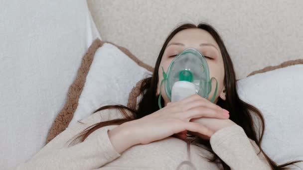 Use nebulizador e inhalador para el tratamiento. Mujer joven inhalando a través de la máscara del inhalador acostada en el sofá. Vista frontal . — Vídeo de stock