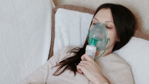 Используйте для лечения ингалятор и распылитель. Молодая женщина вдыхает через маску ингалятора, лежащую на диване. Вид сбоку . — стоковое видео