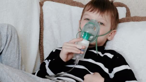 Χρήση του νεφελοποιητή και συσκευή εισπνοής για τη θεραπεία. Αγόρι εισπνοή μέσω της συσκευής εισπνοής μάσκα ξαπλωμένος στον καναπέ. — Αρχείο Βίντεο