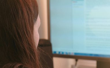 Bilgisayar üzerinde çalışıyor. İnternet sayfalarında ekran tarama tanınmaz halde genç bir kadın. Yan görünüm.