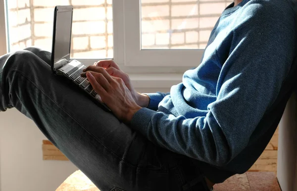 Dolgozik a laptop. Felismerhetetlen fiatal ember gépelés valamit az ő ül az ablak közelében laptop. — Stock Fotó