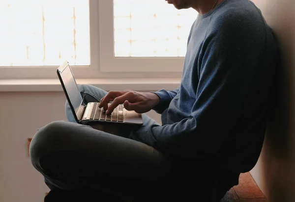 Dolgozik a laptop. Felismerhetetlen fiatal ember gépelés valamit az ő ül az ablak közelében laptop. — Stock Fotó