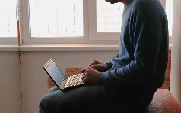 在笔记本电脑上工作。无法辨认的年轻人打开笔记本电脑, 等待它启动坐在阳台附近的窗口. — 图库照片