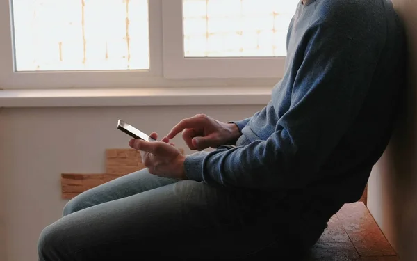 Ο άνθρωπος με το τηλέφωνο. Αγνώριστος νεαρός συνομιλία στο κινητό τηλέφωνο που κάθεται στο μπαλκόνι κοντά στο παράθυρο — Φωτογραφία Αρχείου