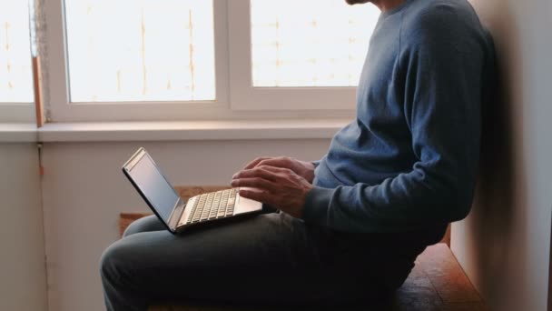 Arbeiten am Laptop. Unbekannter junger Mann öffnet Laptop und wartet auf Balkon am Fenster. — Stockvideo