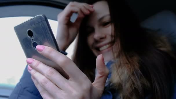 Mujer en un coche con teléfono móvil. Joven hermosa mujer morena buscando algo en el teléfono móvil y y se ríe . — Vídeos de Stock