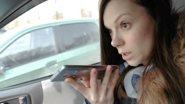Young beautiful woman speak a voice message on a mobile phone sitting in the car. — Stock Video