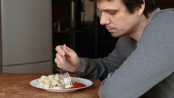 Чоловік їсть пельмені з виделкою, кладе їх у томатний соус на кухні . — стокове відео