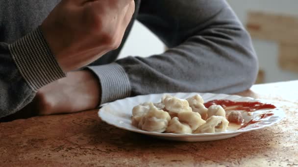 Man eats dumplings with a fork, putting them into tomato sauce in the kitchen — Stock Video