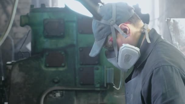 Arbeiter verrichtet seine Arbeit in einer Schutzmaske auf dem Gesicht im Geschäft zwischen den Geräten. — Stockvideo