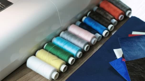 Fils à bobines multicolores, tissu en cuir couché sur la table à côté de la machine à coudre . — Video