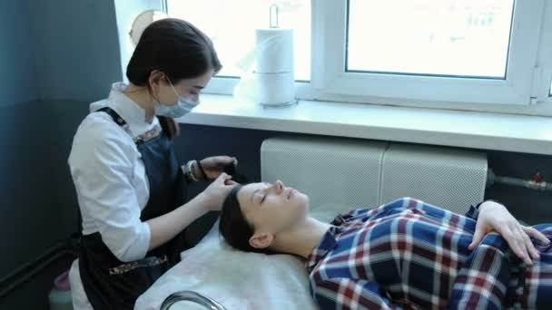 Skönhetsbehandling. Kosmetolog sätter på gummihandskar och förbereder för förfarandet. Kunden ligger på soffan. — Stockvideo