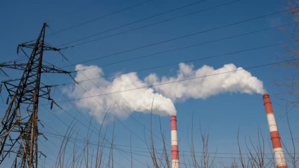 Dos tuberías rojas y blancas de la central térmica con humo en el cielo y fondo de torre de alto voltaje . — Vídeos de Stock