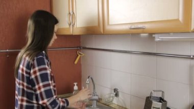 Mutfakta bir bardak yıkama ekose gömlekli uzun saçlı esmer denetler Kupası ve temiz.