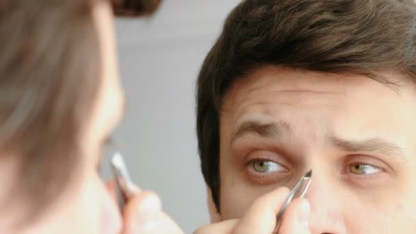 Un jeune homme se pince les sourcils avec une pince à épiler. Sourcils coiffants . — Video