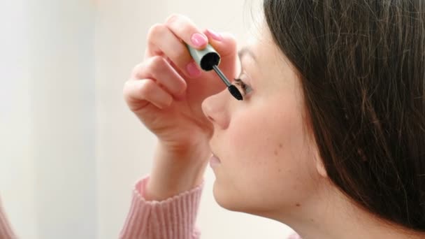 Mooie jonge vrouw schildert haar ogen met mascara. Zijaanzicht. — Stockvideo