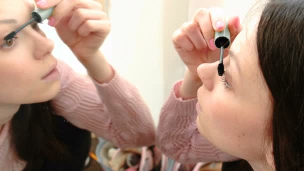 Mooie jonge vrouw schildert haar ogen met mascara voor de spiegel. Zijaanzicht. — Stockvideo