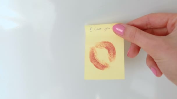 Primeros planos de la mano de las mujeres pegar la nota con un beso y escribir "te amo" en la pared blanca . — Vídeos de Stock