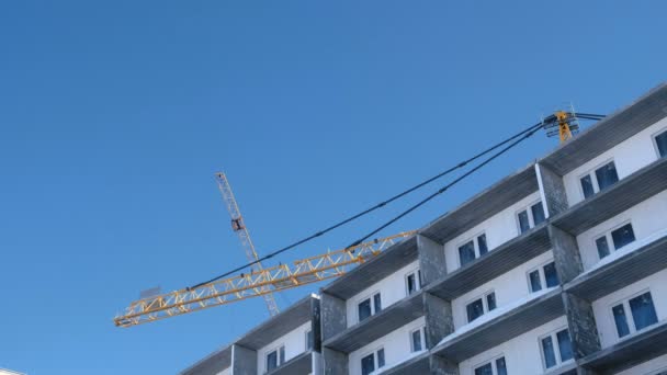 Construction of a multi-storey building. Cranes turns to the side over the roof in sky background. — Stock Video