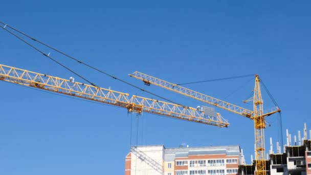 Construcción de edificios de varios pisos. Dos grúas de construcción contra el cielo trabajan en el sitio de construcción . — Vídeos de Stock