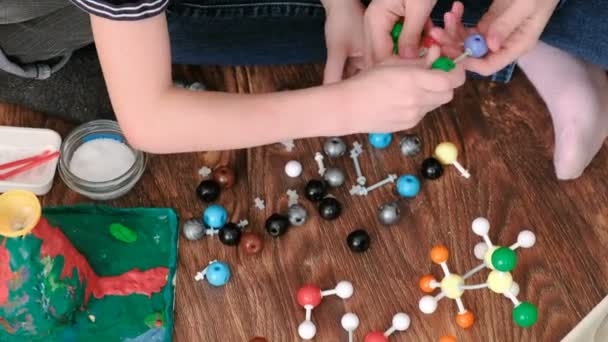 Closeup hands of mom and son building molecule models of colored plastic construction set. Top view. — Stock Video