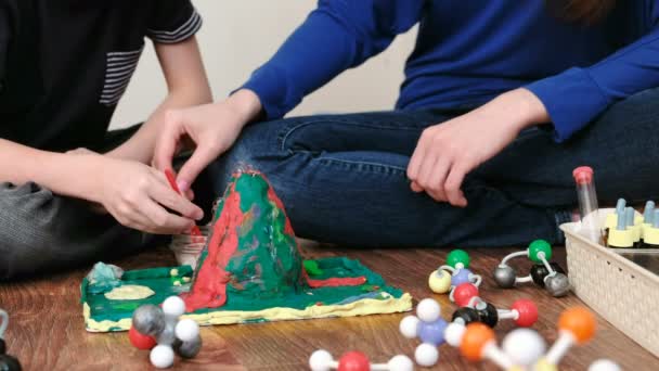 Close-up experience with a volcanic eruption at home. Chemical reaction with gas emission. Mom and son are adding reagents to the plasticine volcano. — Stock Video