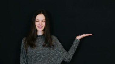 Gülümseyen esmer kadın el palm sağa ve göz üzerinde siyah arka planda gösterir. Metin için yer.