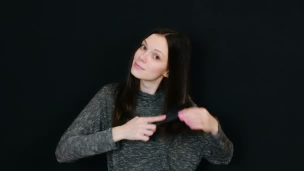 Mujer morena sonriente mirando a la cámara y cepillándose el pelo contra un fondo negro. Espacio para el texto . — Vídeos de Stock