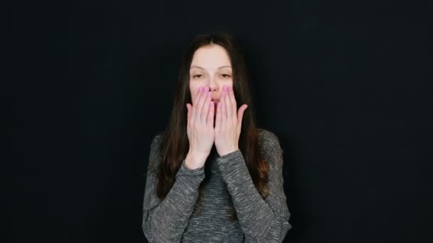 Jonge aantrekkelijke brunette vrouw stuurt een kus van de lucht naar de camera en lachend op zwarte achtergrond. Ruimte voor tekst. — Stockvideo