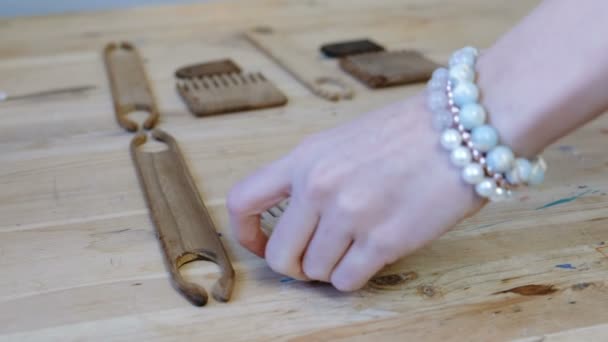 Weaver pone herramientas vieiras y lanzaderas en una mesa de madera en el taller. Primeros planos de las manos de las mujeres con pulseras de cuentas en sus manos . — Vídeos de Stock