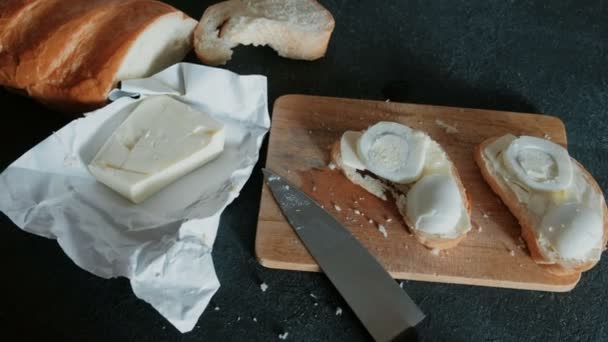 Closeup sandwiches with bread, butter and eggs on wooden board in black background. Making a sandwiches. — Stock Video