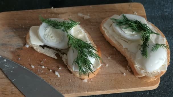Sándwiches de primer plano con pan, mantequilla, huevos y eneldo sobre tabla de madera en fondo negro. Haciendo sándwiches . — Vídeos de Stock
