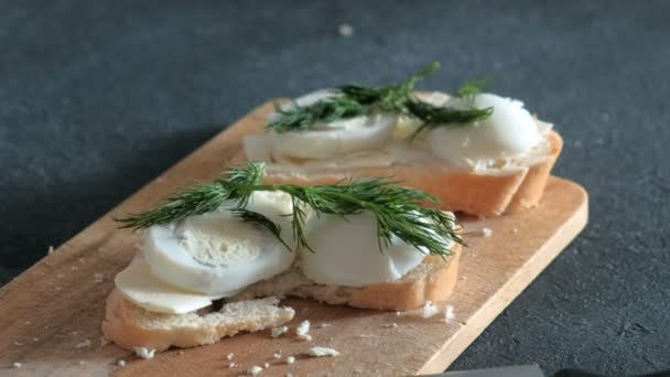 Closeup womans hand neemt een sandwich met brood, boter, eieren en dille uit houten plank op zwarte achtergrond. — Stockvideo
