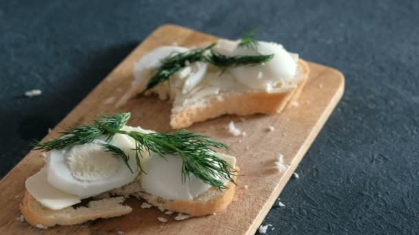 Closeup womans hand neemt een sandwich met brood, boter, eieren en dille uit houten plank op zwarte achtergrond. — Stockvideo