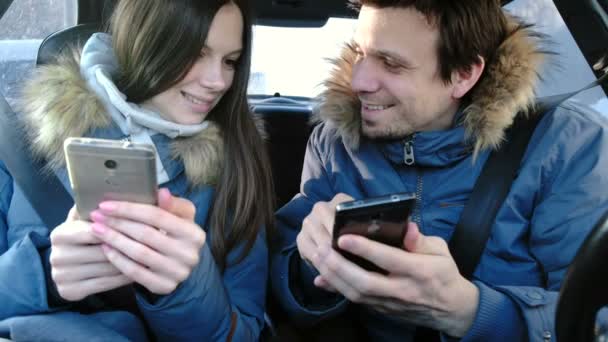 Mann und Frau in ihren Handys und lächelnd im Auto. Frontansicht. — Stockvideo