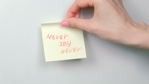 Closeup mulheres mãos furar folhas de papel adesivo amarelo com palavras nunca dizer nunca . — Vídeo de Stock