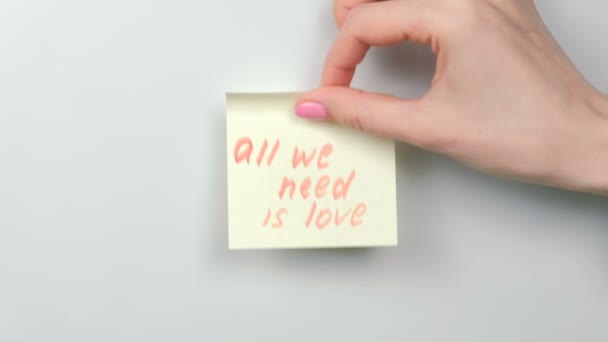 Närbild kvinnans händer stick gul dekal ark med ord alla vi behöver är kärlek. — Stockvideo