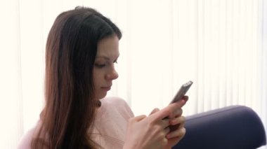 Genç kadın esmer cep telefonu üzerinde tipik bir haber ve ekrana bakarak. Yan görünüm.
